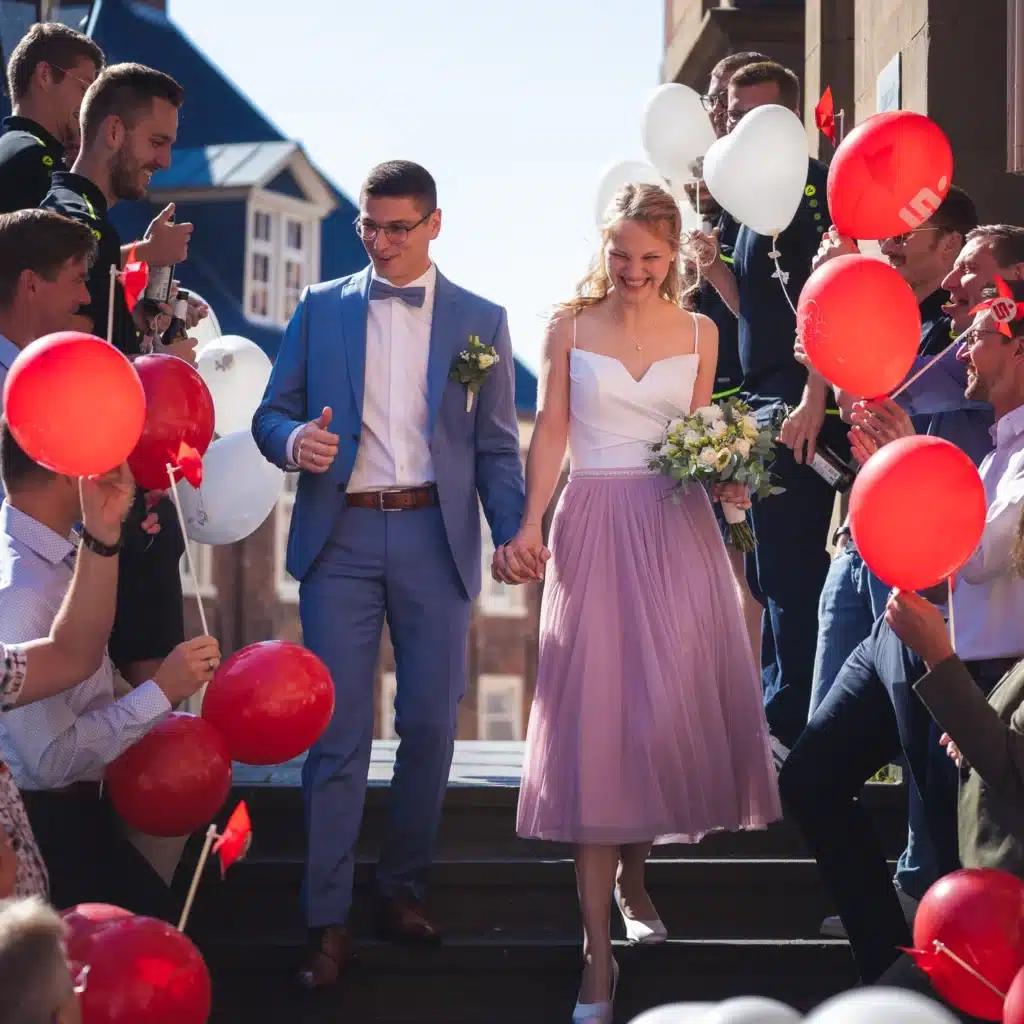 Brautpaar verlässt das Standesamt, umgeben von Gästen mit roten und weißen Luftballons.