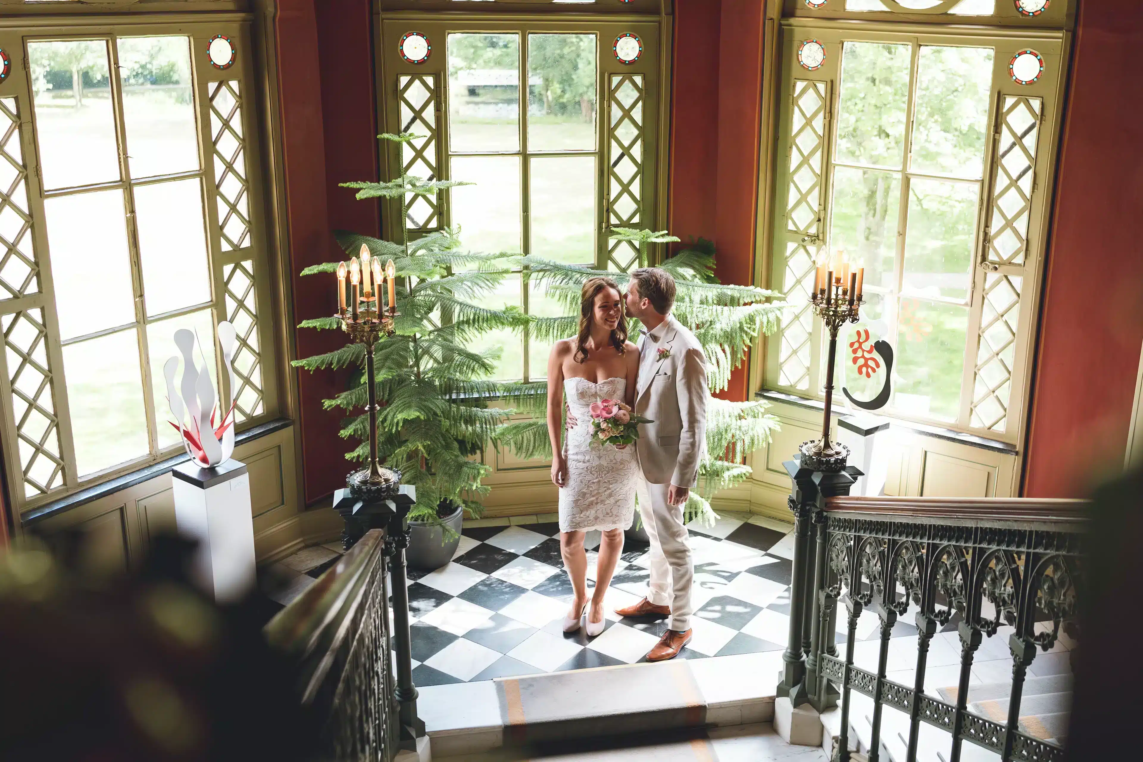 Thomas und Elena bei ihrer standesamtlichen Hochzeit im Schloss Evenburg in Leer, stehend auf einer Treppe und lächelnd.