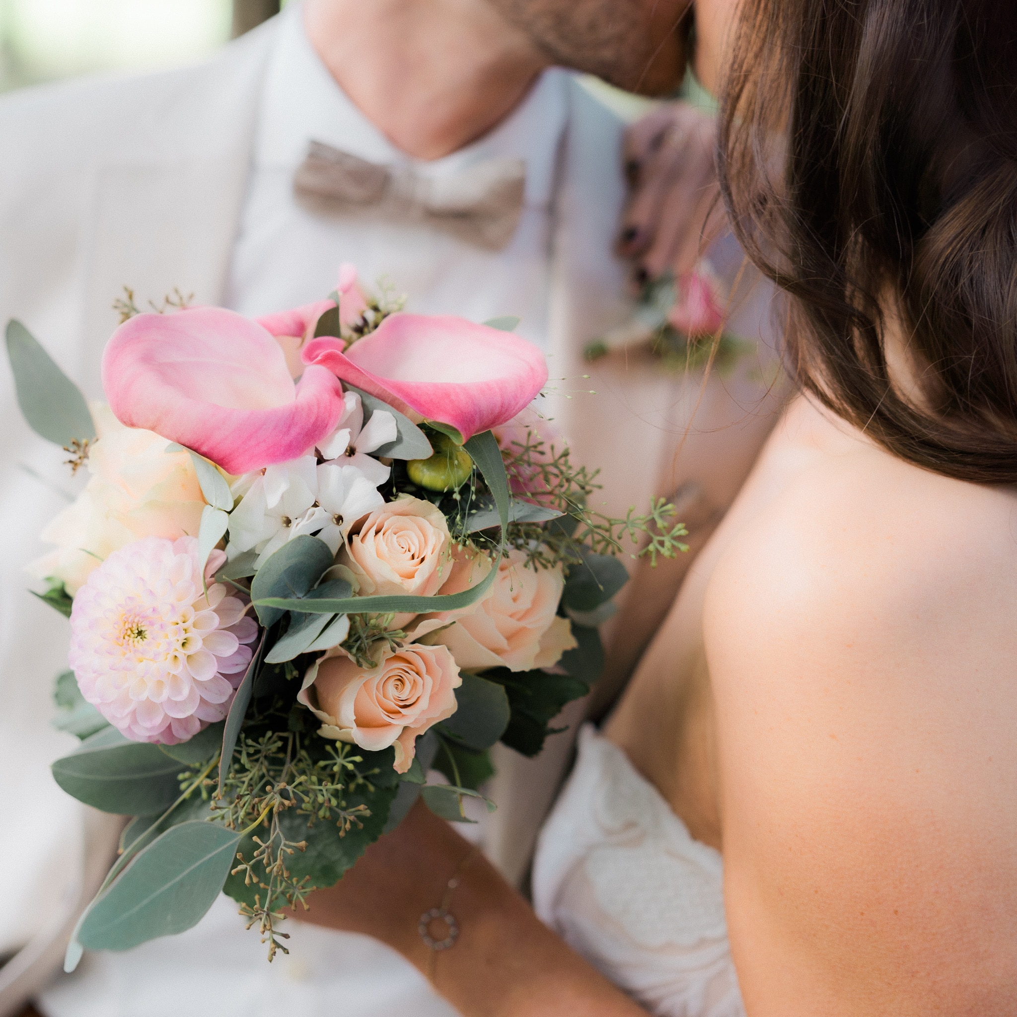 Ein Brautpaar teilt einen intimen Moment und hält einen Blumenstrauß mit rosa und cremefarbenen Blumen.