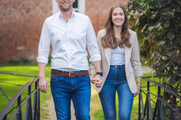 Jan und Lena gehen Hand in Hand auf einer Brücke im Garten vom Gut Altenkamp in Aschendorf.