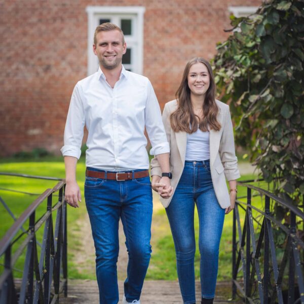 Jan und Lena gehen Hand in Hand auf einer Brücke im Garten vom Gut Altenkamp in Aschendorf.