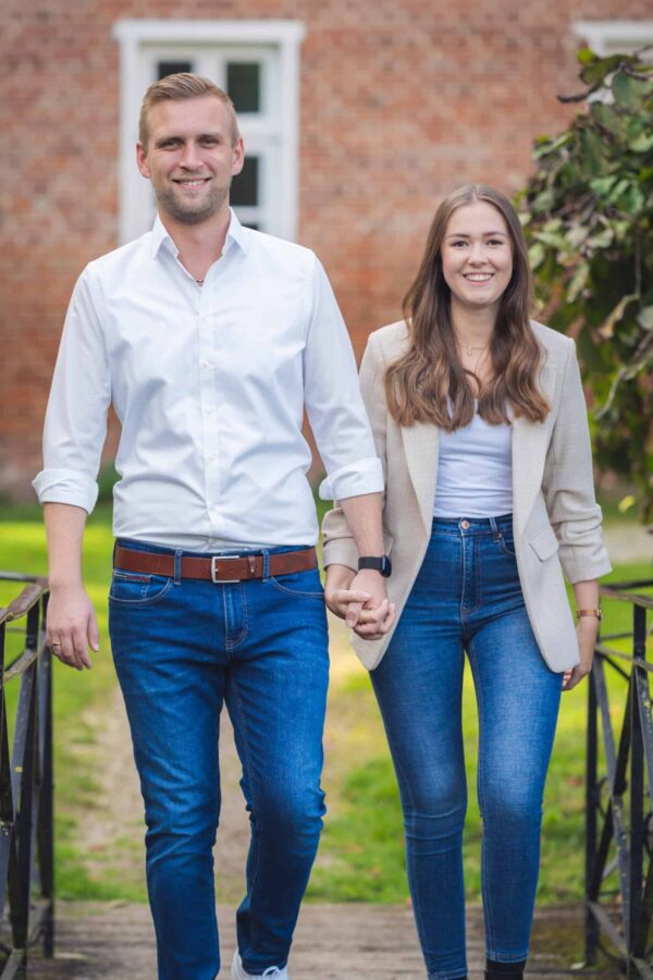 Jan und Lena gehen Hand in Hand auf einer Brücke im Garten vom Gut Altenkamp in Aschendorf.